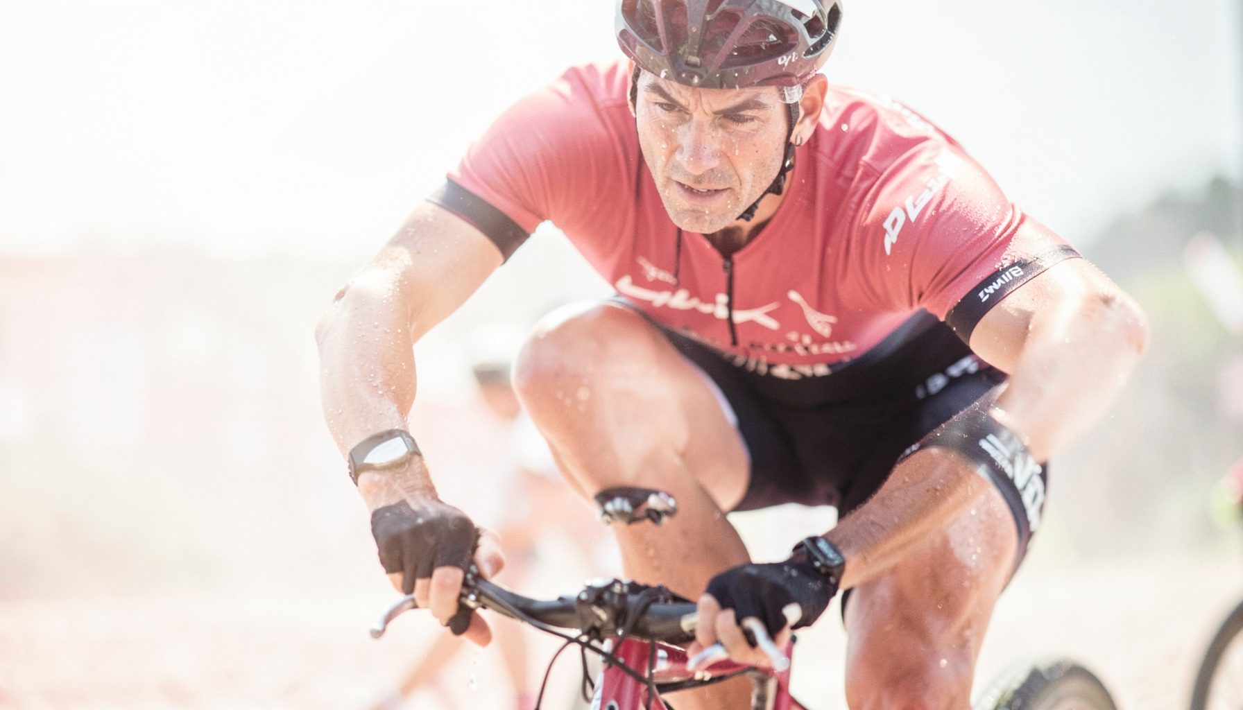 A rider pushing hard on the pedals, sweat glistening, intense focus during a Zwift race, dramatic side lighting